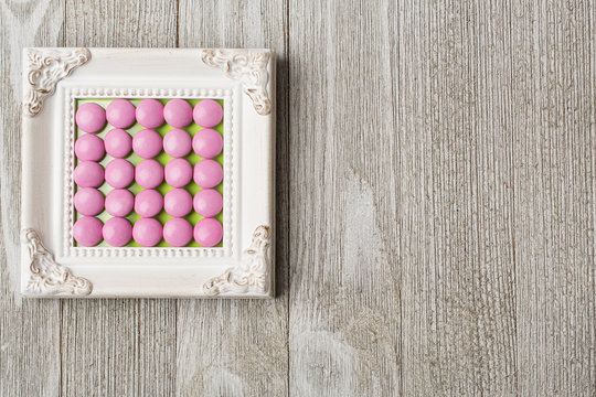 Vintage white frame with pink circle candy arranged in the center.