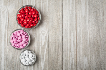 Three bowls of red, pink, white candy arranged on white painted board.