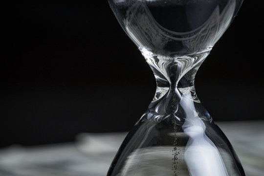 Closed up of sandglass or hourglass with reflection of US dollar banknotes on black background using as time investment or financial deadline concept