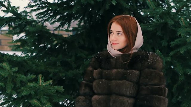 Close-up of Brunette fashionable sexy pretty rich woman or glamour model girl with beautiful long hair in waist coat of brown fur in scarf walking in winter on background of Christmas tree and posing