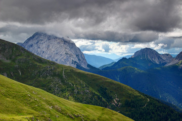 Green hills and rocky ridges of Carnic Alps with towering giant limestone Monte Peralba Hochweissstein peak capped with dark low storm clouds Veneto / Friuli Venezia Giulia Northern Italy Europe