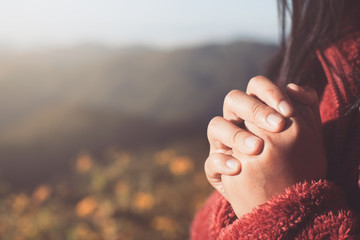Woman hands folded in prayer in beautiful nature background with sunlight in vintage color tone - obrazy, fototapety, plakaty