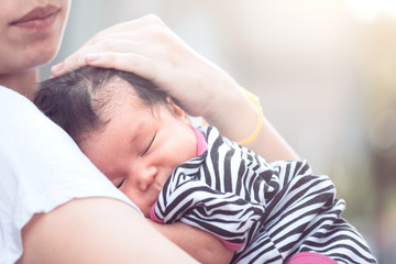 Cute asian newborn baby girl sleeping on mother's chest. Young mother cuddling baby with tenderness.