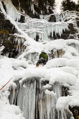 male ice climber in a green jacket on a frozen waterfall in the Swiss Alps