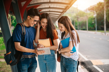 A group of young or teen Asian student in university smiling and reading the book and look at the tablet or laptop computer in summer holiday.