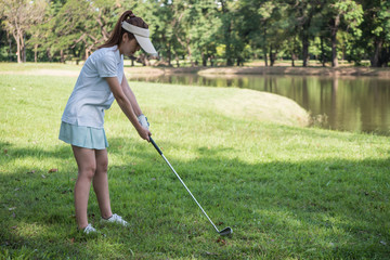 Asian woman golf player swinging driver golf club on golf course.