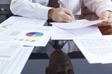 Partially cropped of business man signing his signature on a document with face reflection on the...