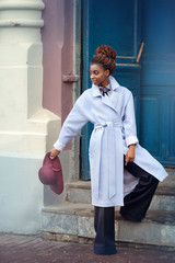 African girl on the street in a blue coat holding a Burgundy hat and looking inside