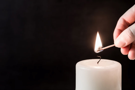 Hand ignite a white candle with match stick on the dark background. Condolence and religion concept. Empty place for a text.