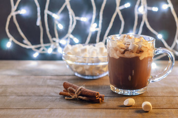 Hot chocolate, cinnamon sticks and marshmallow on the background of burning garlands, Christmas decorations, close up