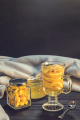 Tea with ginger and lemon in a glass cup and yellow sweets on a wooden background