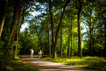 Man and woman cycling away from the camera through a leafy green forest along a dirt road in summer