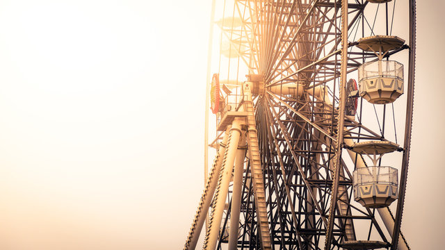 Close up view of the gondolas suspended from the rim of a ferris wheel lit by the warm glow of the sun at an amusement park with copy space - Powered by Adobe