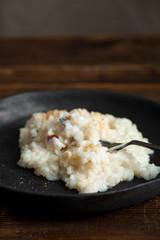Traditional creamy tender risotto with spicy breadcrumbs in black ceramic plate on wooden table. Closeup image, side view.