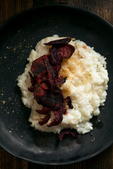 Traditional creamy tender risotto with spicy breadcrumbs and baked savoury beetroot slices in black ceramic plate on wooden table. Vertical composition, closeup shot from above.