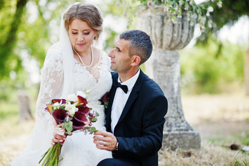 Attractive bride sitting on the groom's lap outdoor on the wedding day.