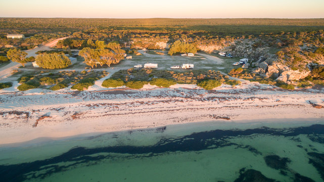 Aerial view of four wheel drive vehicles and caravans at a free camp next to a beach and cliffs in the late afternoon