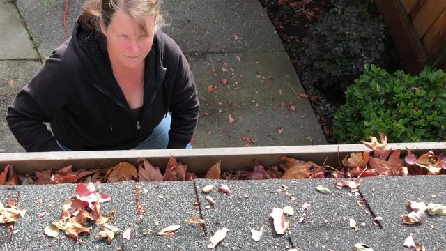 4K HD video of Older female on a ladder cleaning autumn leaves out of rain gutters. A debris clogged gutter can cause a leaky roof or water damage to the interior or exterior of your home.