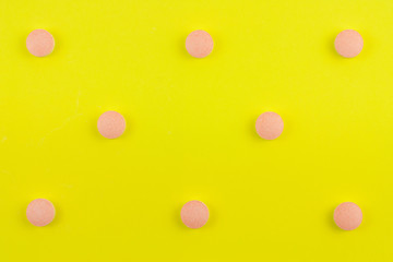 Scattered whole white and pink pills on background of yellow paper. Top view