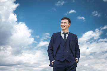 Handsome asian groom in a dark blue smiling against the backdrop of beautiful sky. concept of a strong successful man