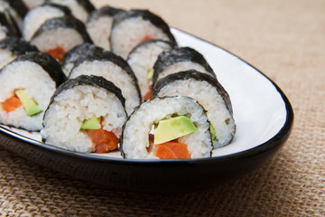 Sushi rolls in nori seaweed with avocado and red fish on ceramic plate