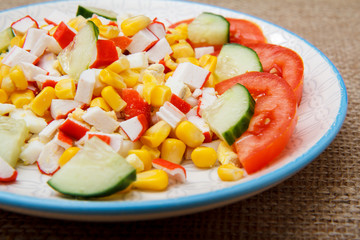 Salad with crab sticks, boiled corn and freshly sliced tomato and cucumber on plate