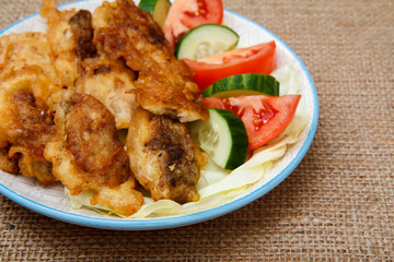 Plate with pieces of fried fish and freshly sliced tomatoes and cucumbers