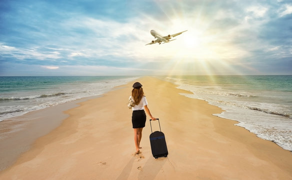 Travel Concept. Young Woman In Office Clothes Walking On The Beach With Suitcase And Hat . Overhead Fly Plane.