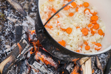 Fototapeta na wymiar Boiling, hot goulash soup with meat, paprika, potatoes, onion, carrots is the traditional dish of Hungarian cuisine. Meat stew being prepared in crock pot on open fire. Picnic at the weekend in nature