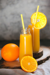 Still life of two bottle full of orange juice and sliced fruits.