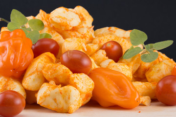 Habanero cheese curds with fresh peppers and tomatoes on a wooden cutting board on a black background