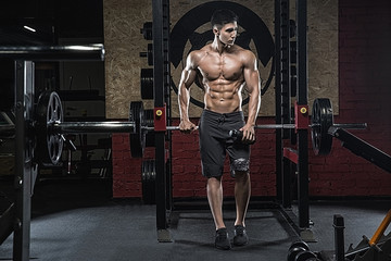 A young handsome, well-muscled Asian man, standing near the leg trimming machine, holds a sports shaker in his hand.