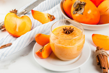 Persimmon fruit smoothie with cinnamon and anise stars, white marble table copy space