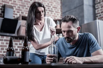 Foto op Canvas Alcoholic in a family. Brutal bearded sad man sitting in front of the vodka bottle and thinking about his problems while drinking at home © zinkevych