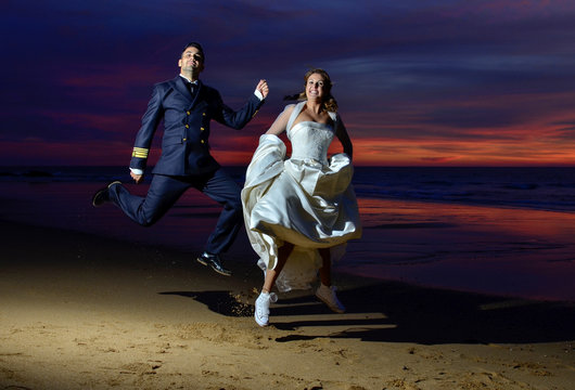 Pareja de recién casados saltando en la playa por la noche