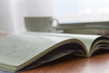 open magazine with a stack of old magazines and a Cup of coffee on the table