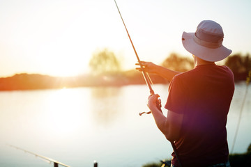 Fototapeta Young man fishing on a lake at sunset and enjoying hobby obraz