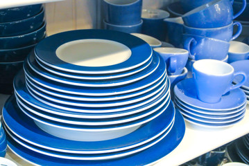 Bright blue and white dishes, plates and cups standing on white shelf. Concept of buying choosing new dishes for house home, interior indoor decoration o for gifts. Clean ordered dishes in store.