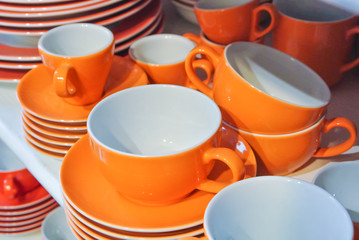 Bright orange and white dishes, plates and cups standing on white shelf. Concept of buying choosing new dishes for house home, interior indoor decoration o for gifts. Clean ordered dishes in store.