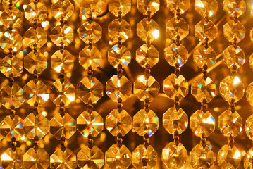 Bright golden gold yellow shiny abstract pattern, close up of details of a big beautiful luxury crystal chandelier, abstract indoor background with blur bokeh at the background.