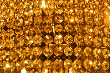 Bright golden gold yellow shiny abstract pattern, close up of details of a big beautiful luxury crystal chandelier, abstract indoor background with blur bokeh at the background.