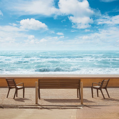 Beautiful panoramic view to benches standing in front of the sea shore coastline bay beach, blue transparent sea ocean waves and cloudy sky. A place for relax and vacations in a town by the sea water.
