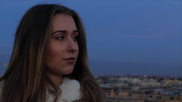 Beautiful red-haired student female thoughtfully gazing the sunset of Roman city on the terrace in the centre of mega polis. European woman with an adorable look dressed in fur coat