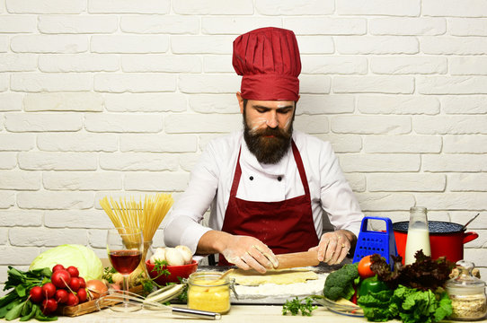 Cook with serious face in burgundy uniform sits by table