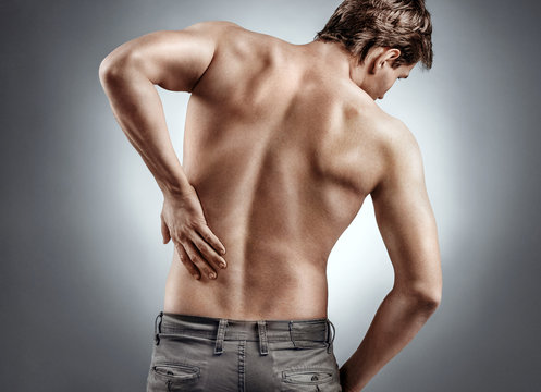 Man holding his back in pain on grey background. Medical concept