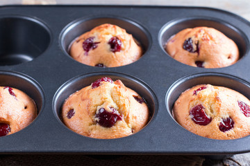 Homemade muffins with cherry in a baking form on a wooden background
