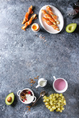 Breakfast set with smoked salmon on crispy breadsticks, yogurt, smoothie, avocado, muesli, milk, berries and green grape over blue texture background. Top view, copy space. Food background