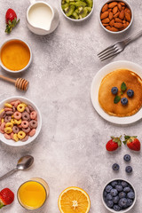 Breakfast with colorful cereal rings, pancakes, fruit, milk, juice.