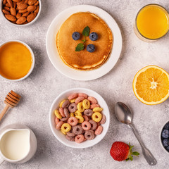 Breakfast with colorful cereal rings, pancakes, fruit, milk, juice.