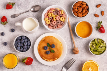 Breakfast with colorful cereal rings, pancakes, fruit, milk, juice.